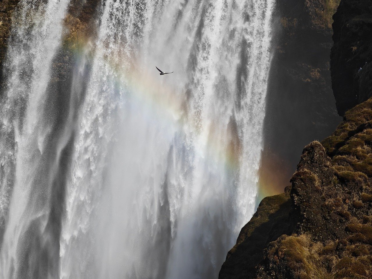 Waterfall mist creating rainbow with hiker