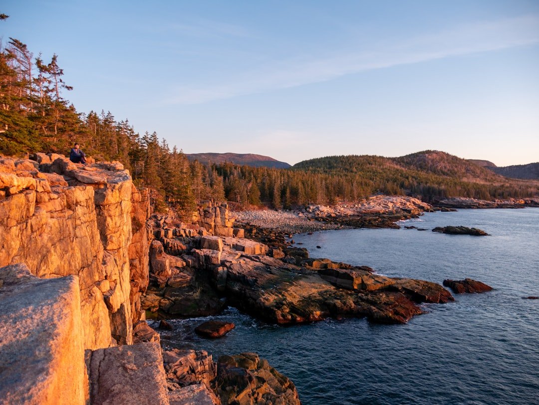 Hiker navigating rocky coastal trail with ocean views along Acadia's rugged shoreline