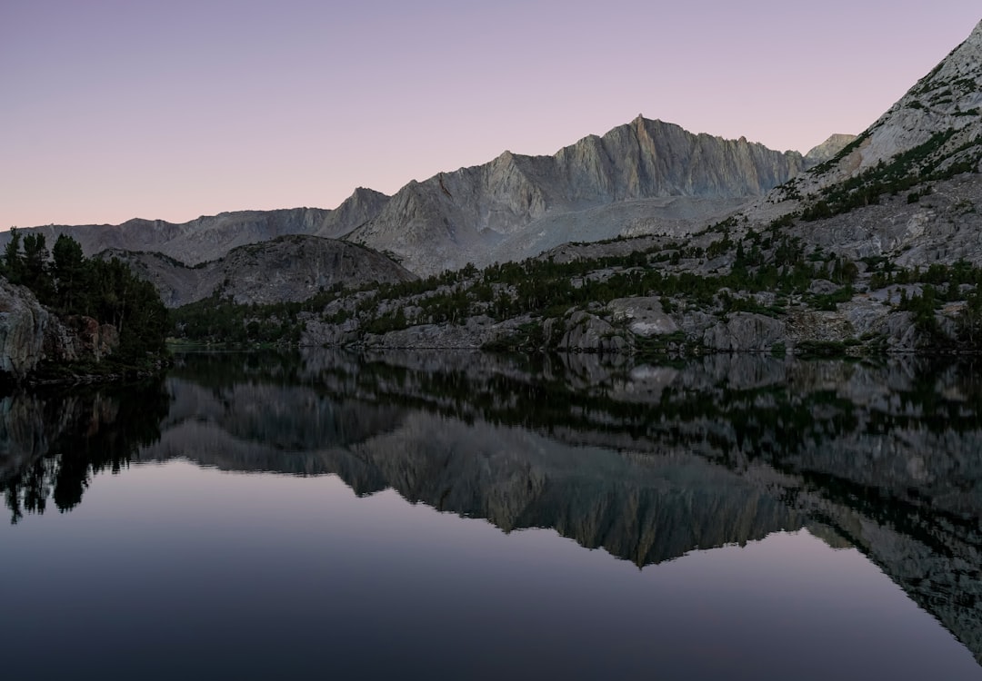 Glassy mountain lake reflecting surrounding peaks at sunrise