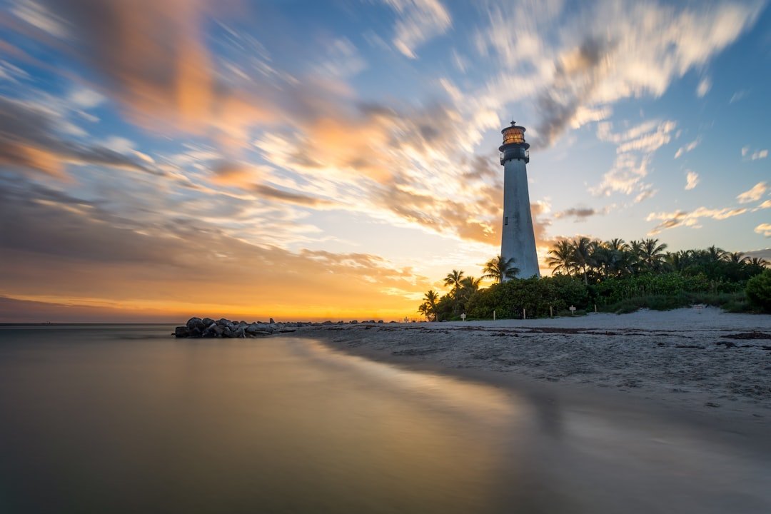 Lighthouse standing above palm-lined beach at sunset