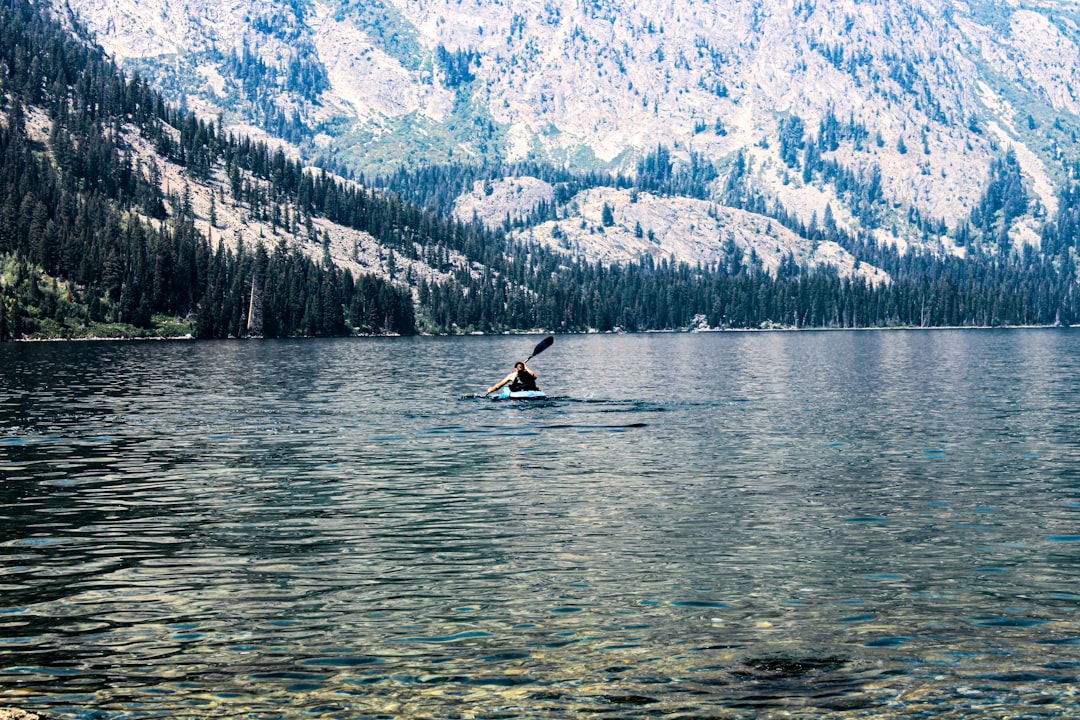 A kayaker paddling a calm mountain lake with peaks reflected in the water