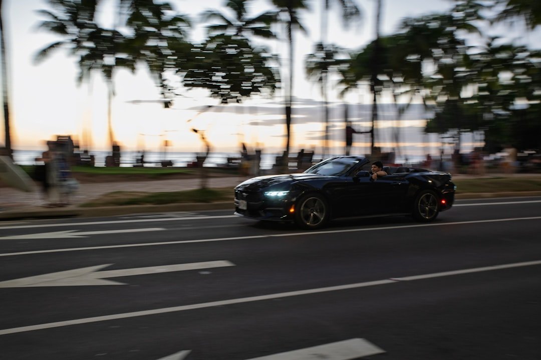 Convertible driving coastal road at dusk with palm trees