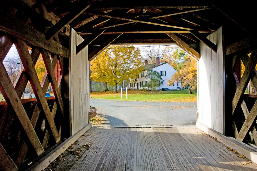 View from inside a covered bridge framing a farmhouse amid yellow fall trees