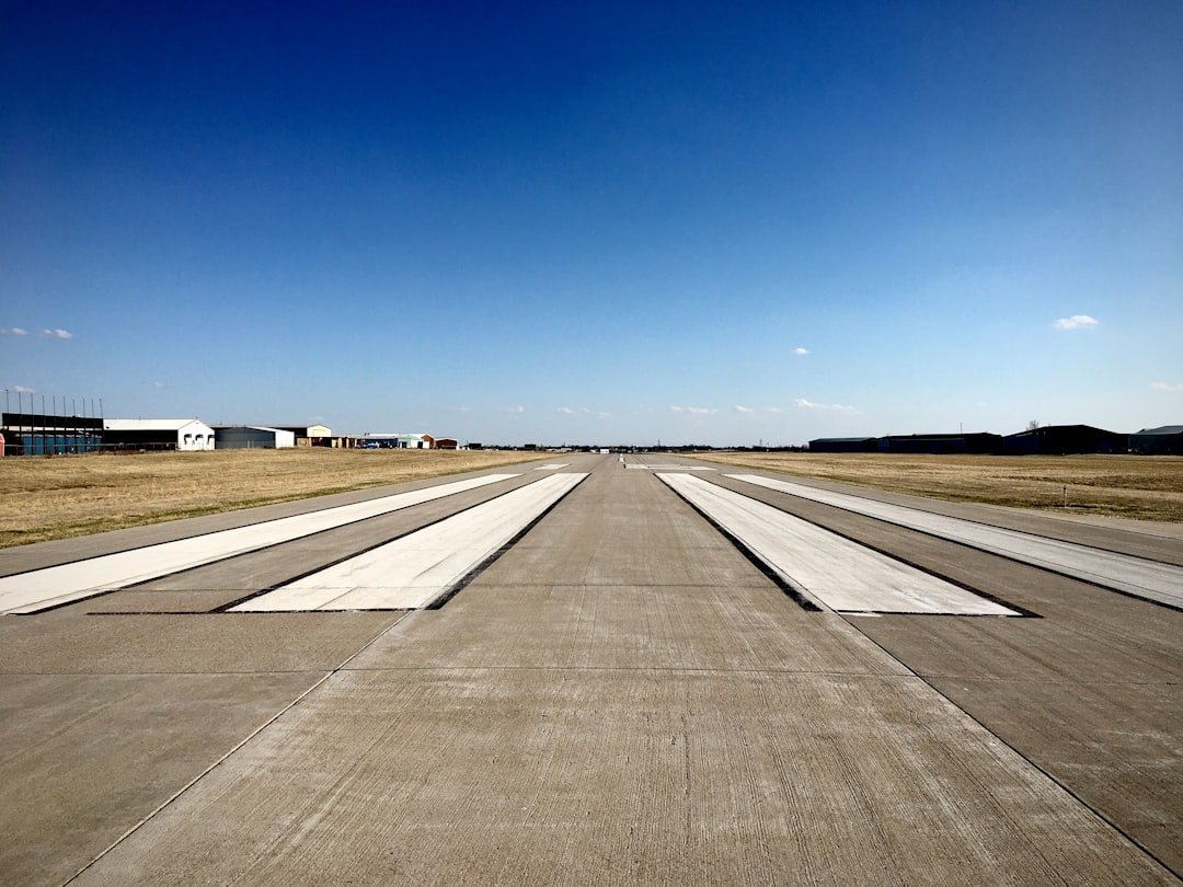 A quiet runway stretching into the distance at a small airport, hangars and fields beyond