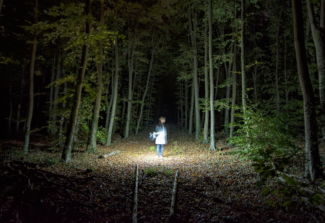Hiker holding a lit headlamp on a dark autumn forest trail