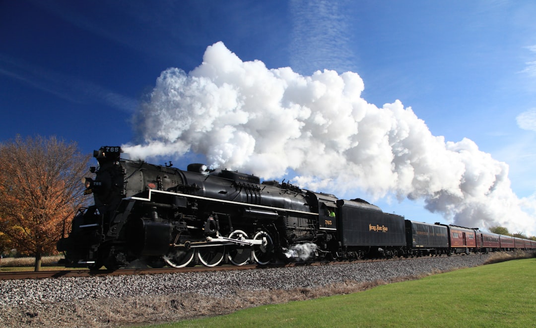 Steam locomotive billowing white smoke through autumn countryside