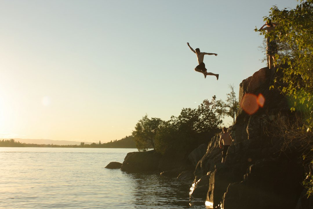 A swimmer leaping from a rock ledge into a lake at sunset