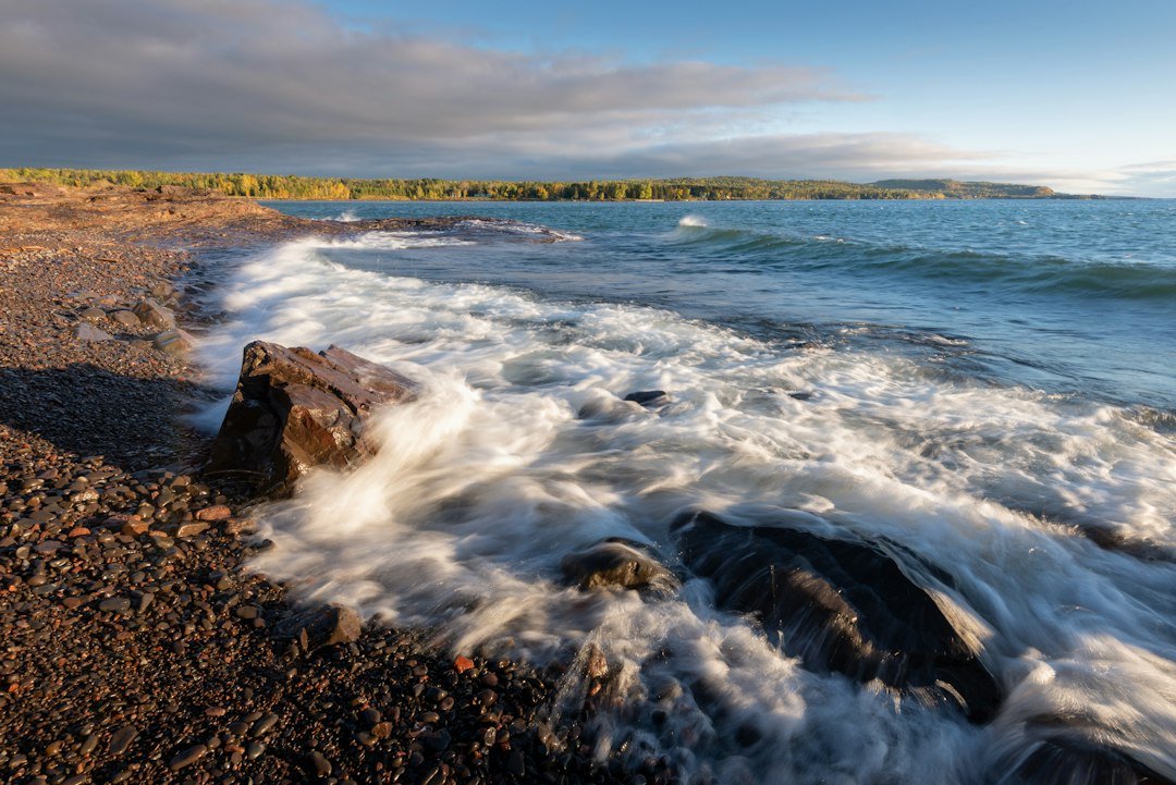 Waves crashing against a rocky shoreline with cliffs in the distance