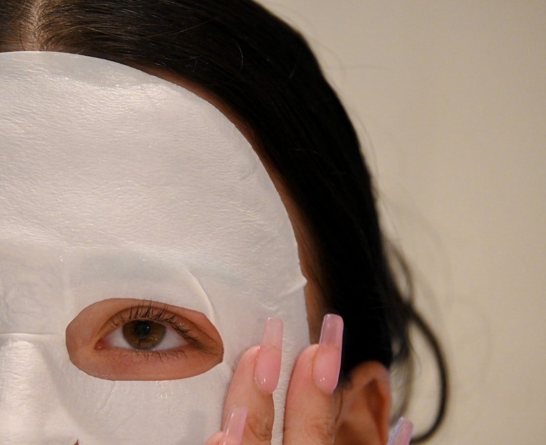 Woman wearing a white skincare sheet mask, smoothing it into place