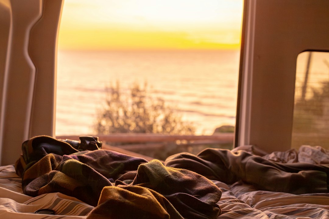 Cozy rumpled blankets on a campervan bed with the door open at sunset