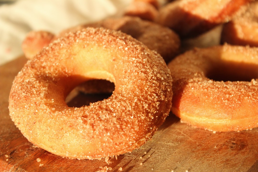 Apple cider donuts coated in cinnamon sugar on a wooden surface