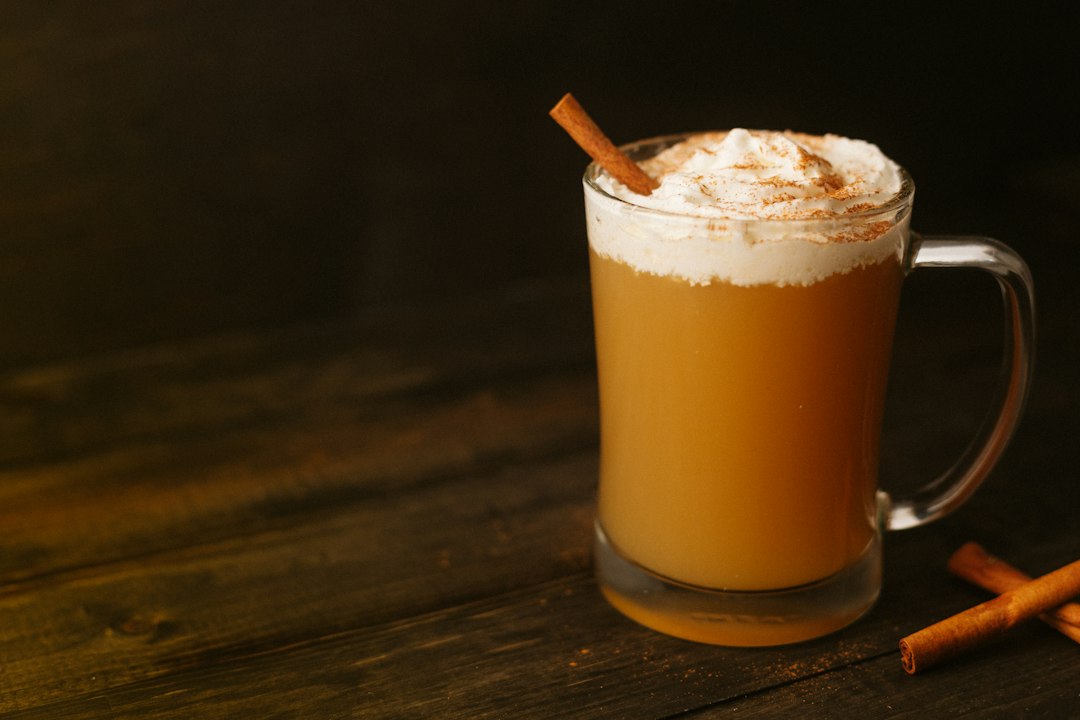 Glass mug of hot apple cider topped with whipped cream and a cinnamon stick