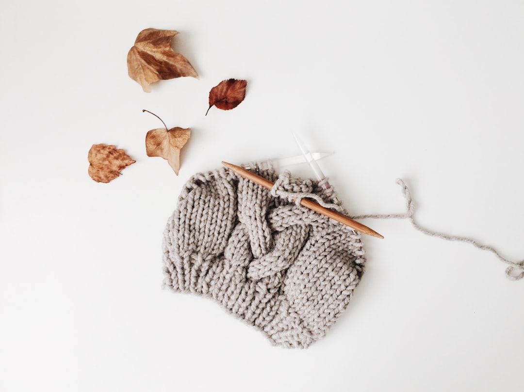 Knit merino beanie beside knitting needles and autumn leaves