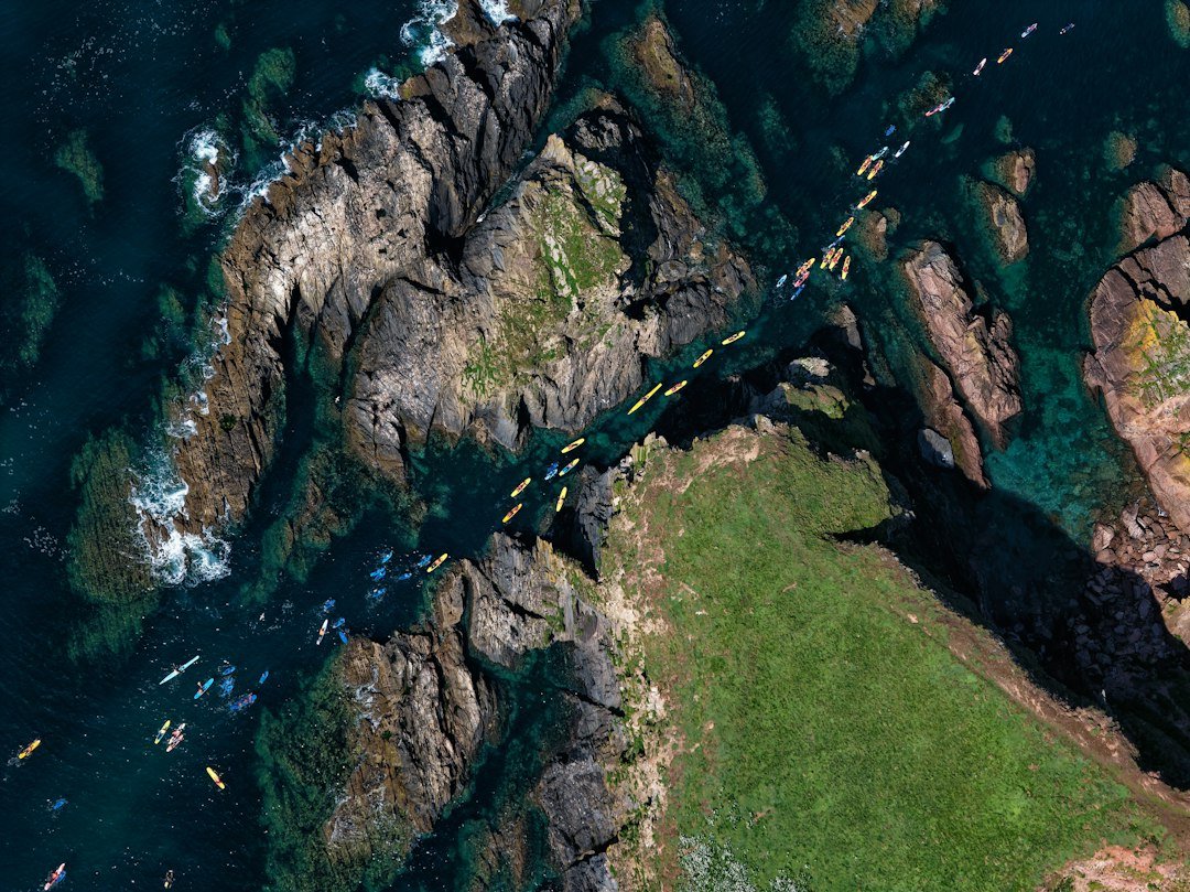 Kayakers paddling along a rocky coastline in clear water