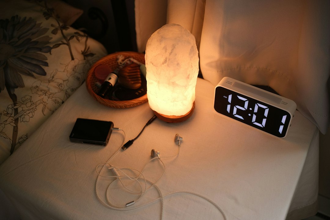 Nightstand with digital alarm clock and charging earbuds beside the bed