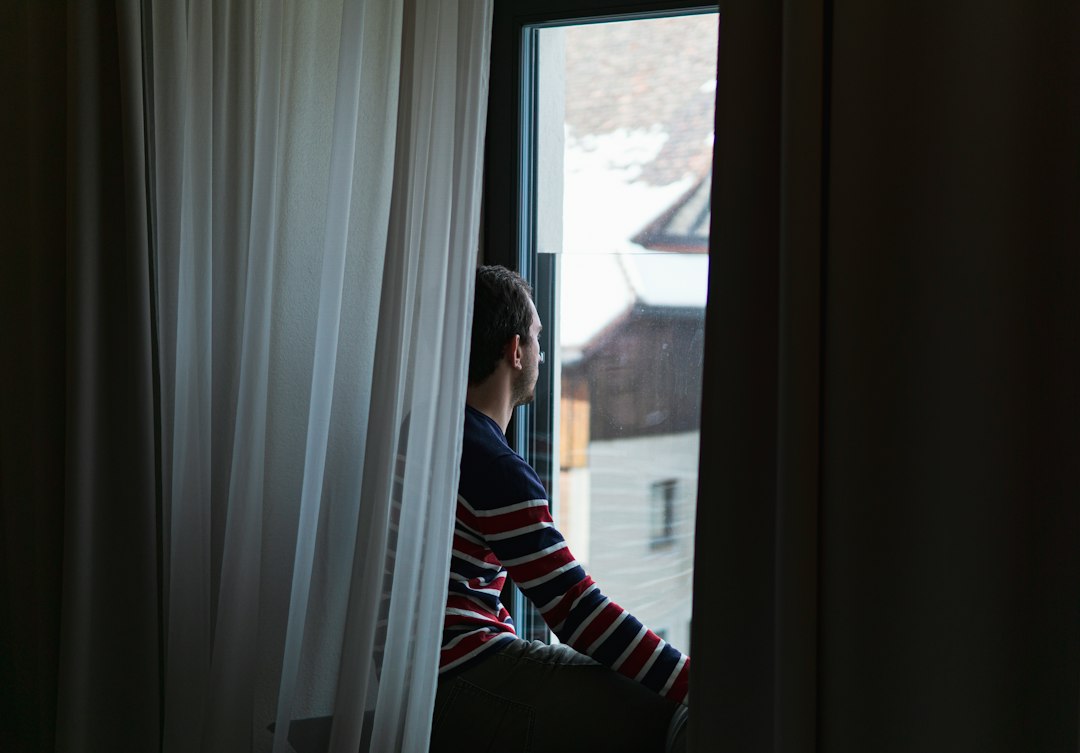 Traveler sitting on a snowy hotel windowsill watching snow-covered rooftops