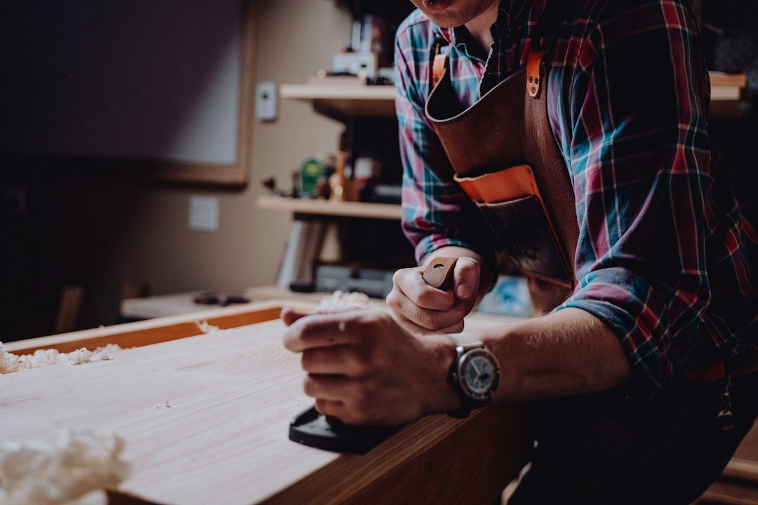 Woodworker planing a board at a workbench while measuring a project