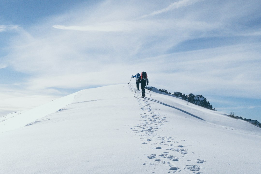 Two hikers with poles crossing a snowy ridge