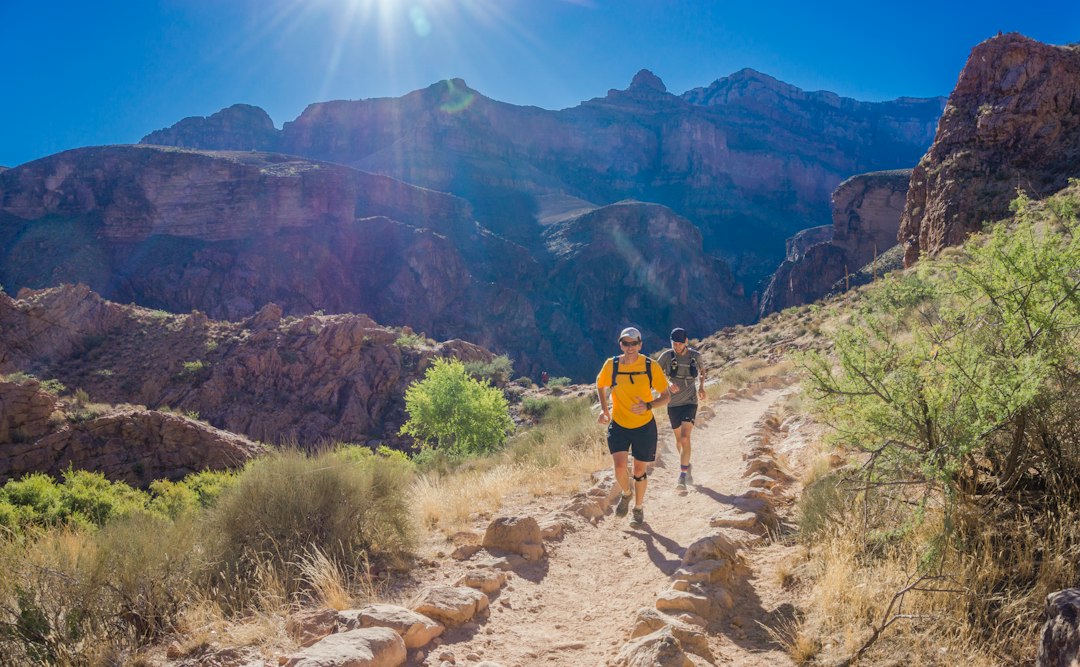 Two hikers walking a rocky trail through a sunlit desert canyon