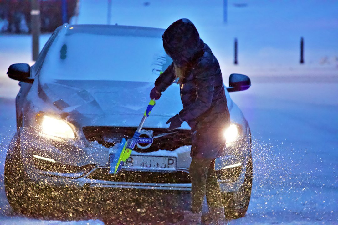 A driver brushing snow off a car windshield at night