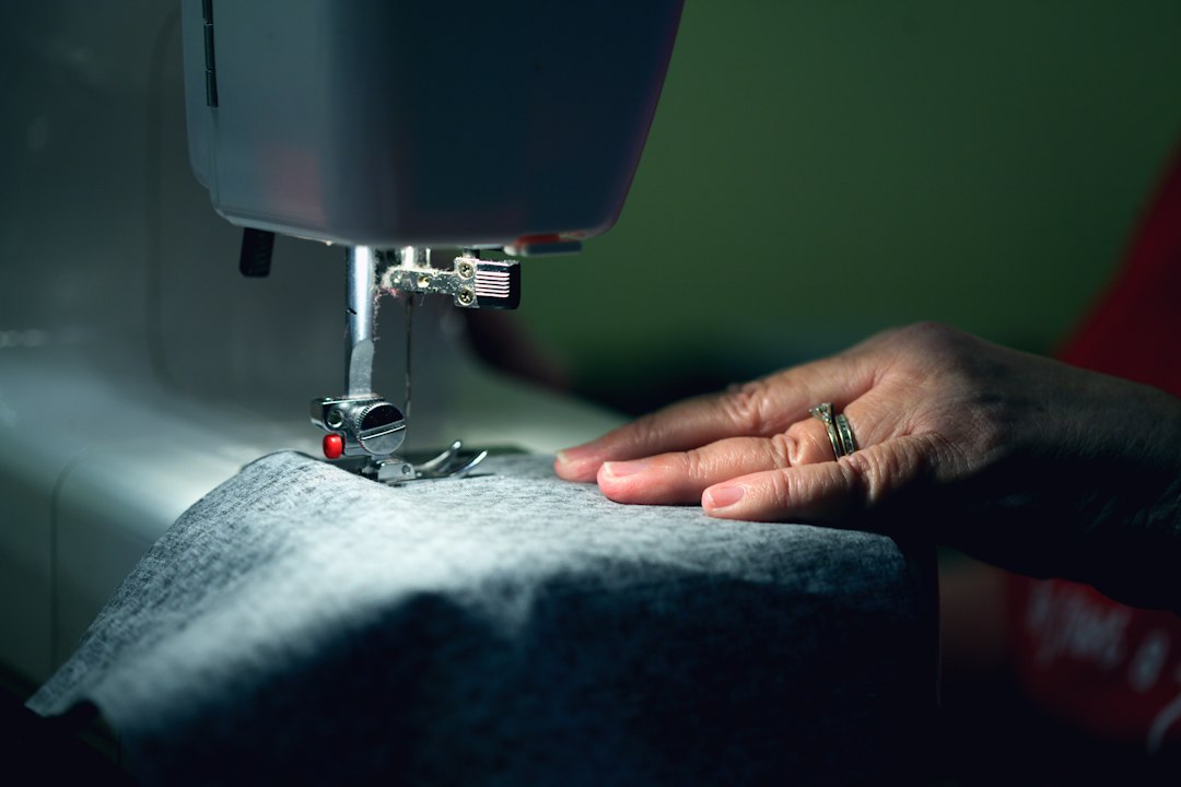 Hands guiding gray fabric through a sewing machine
