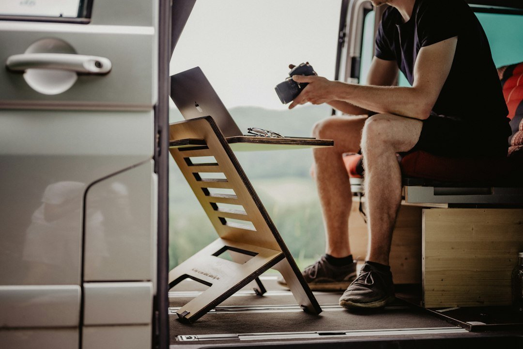 Working on a laptop at a wooden surface inside a van with hills outside the door