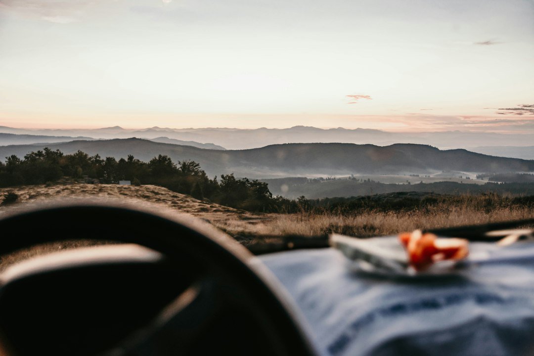 Plate of food on a surface inside a vehicle overlooking misty mountains at sunset