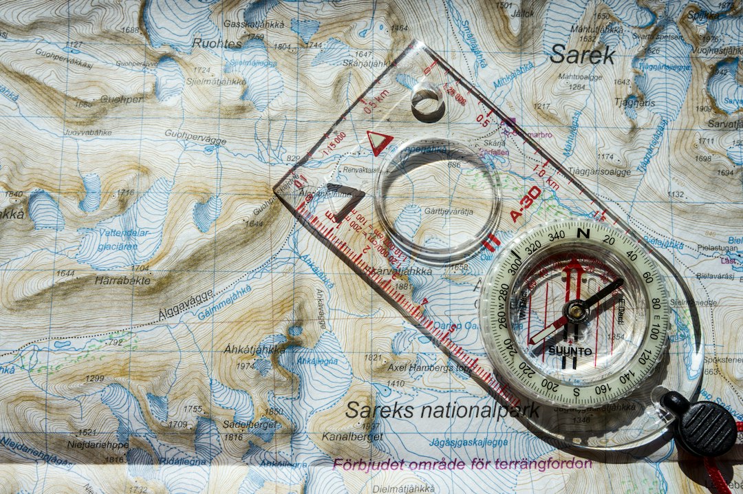 Backpacker studying a paper map with a communicator clipped to the pack strap
