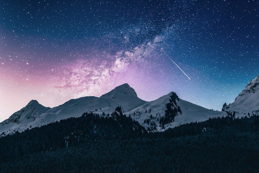 A meteor streaks over snow-capped mountains under a star-filled night sky