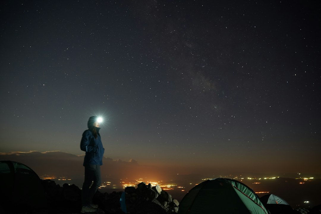Camping tent under a brilliant starry night sky with a distant headlamp glow
