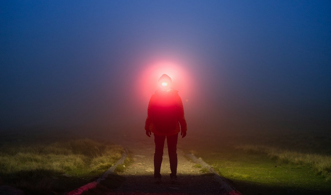 A red headlamp cutting through night fog on a dark trail