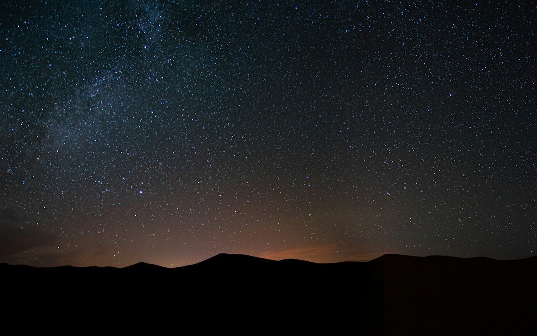 The Milky Way arching over dark desert hills on a moonless night