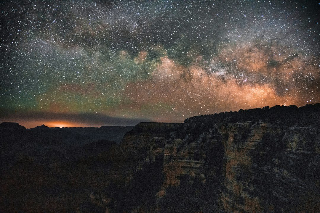 The Milky Way arching over dark canyon cliffs on a moonless night