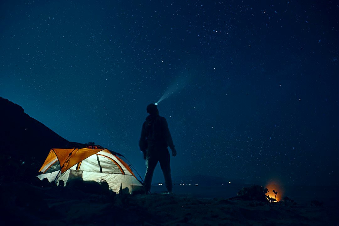 A traveler holding a light outside a tent under a starry sky